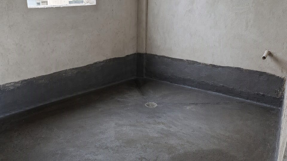 A bathroom under construction with a dark waterproof coating on the floor and lower walls and a floor drain at the low point