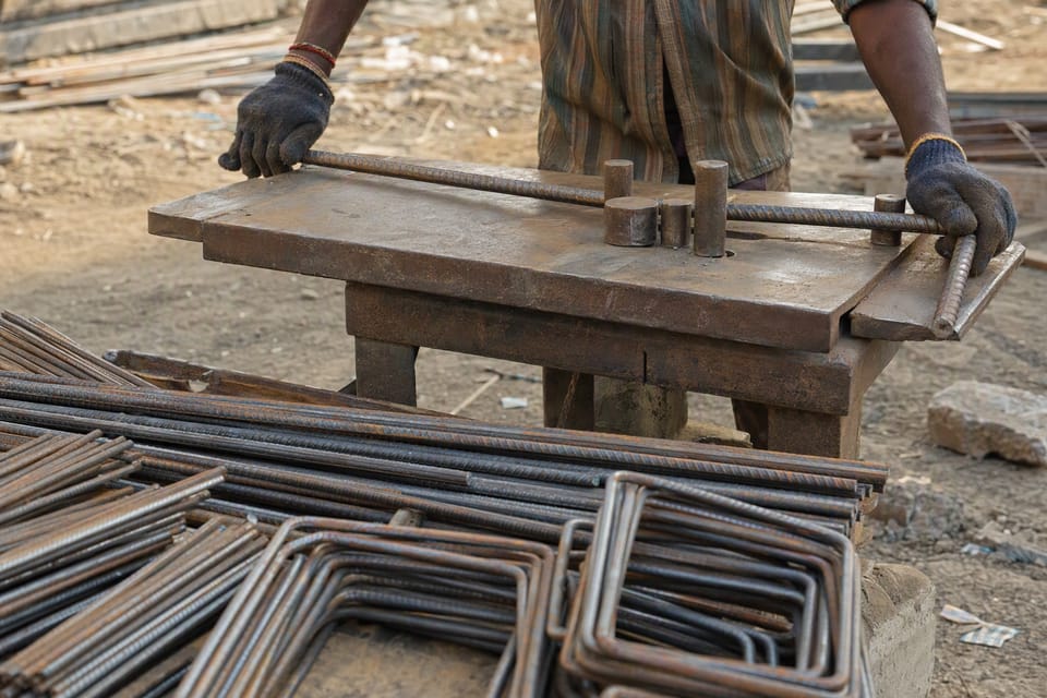 A worker bending a steel bar on a bending table, with cut bars and bent stirrups in front