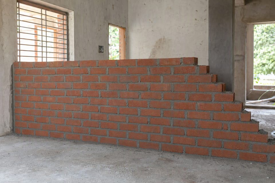 A half-built brick partition wall in stretcher bond, with its unfinished end stepped back like a staircase
