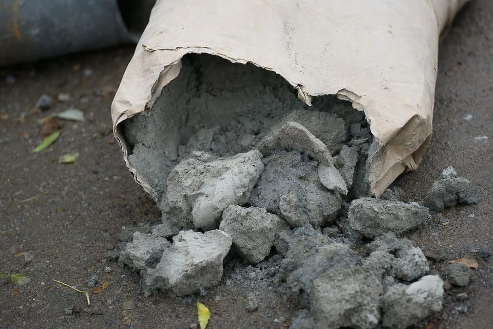 Hard grey lumps of cement spilling from a torn paper bag on damp ground