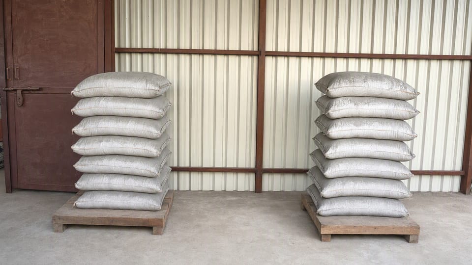Two stacks of plain grey cement bags standing on wooden pallets on a clean concrete floor in a covered shed