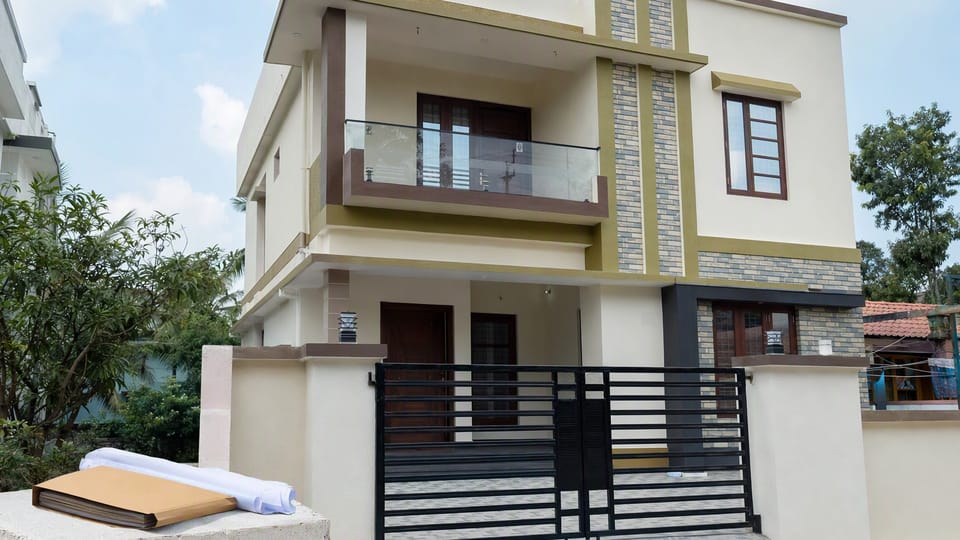A newly completed two-storey house with a closed gate, and a document folder and rolled drawings resting on the front wall