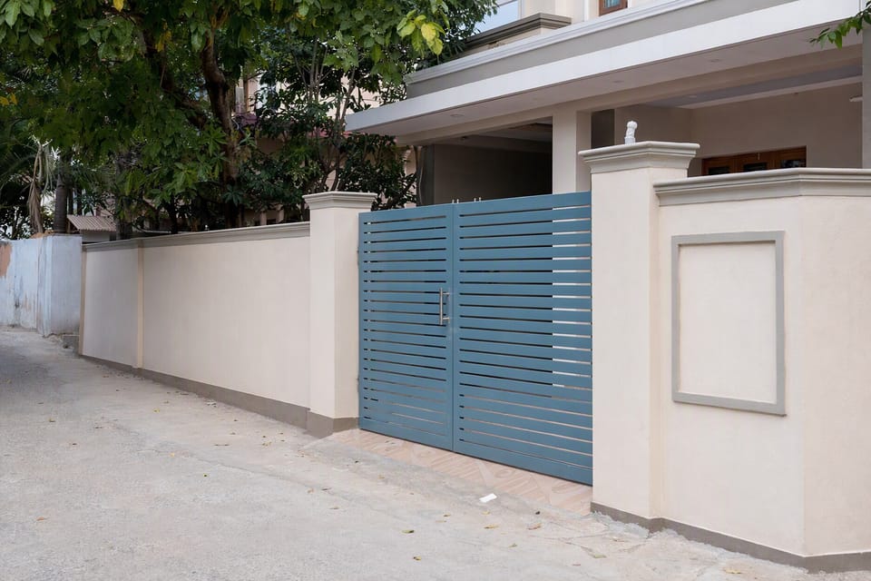 A plastered compound wall with square pillars and a metal gate