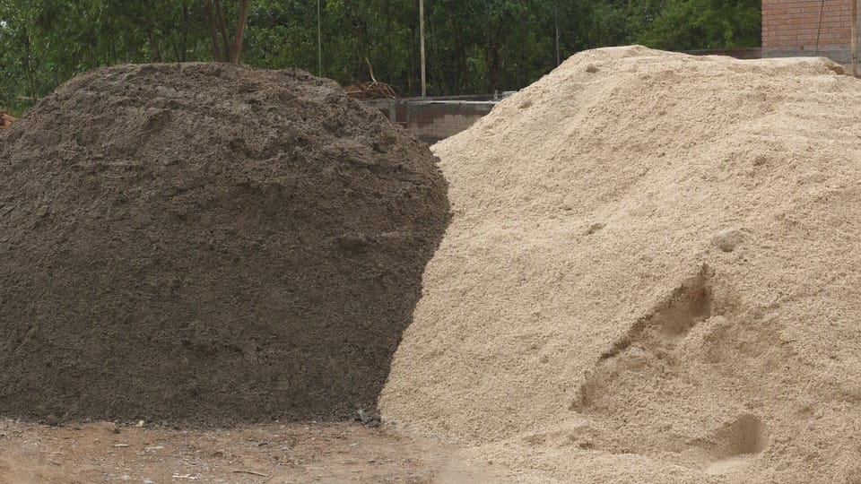 Two heaps of sand side by side on a building site, one dark and damp and the other pale and dry