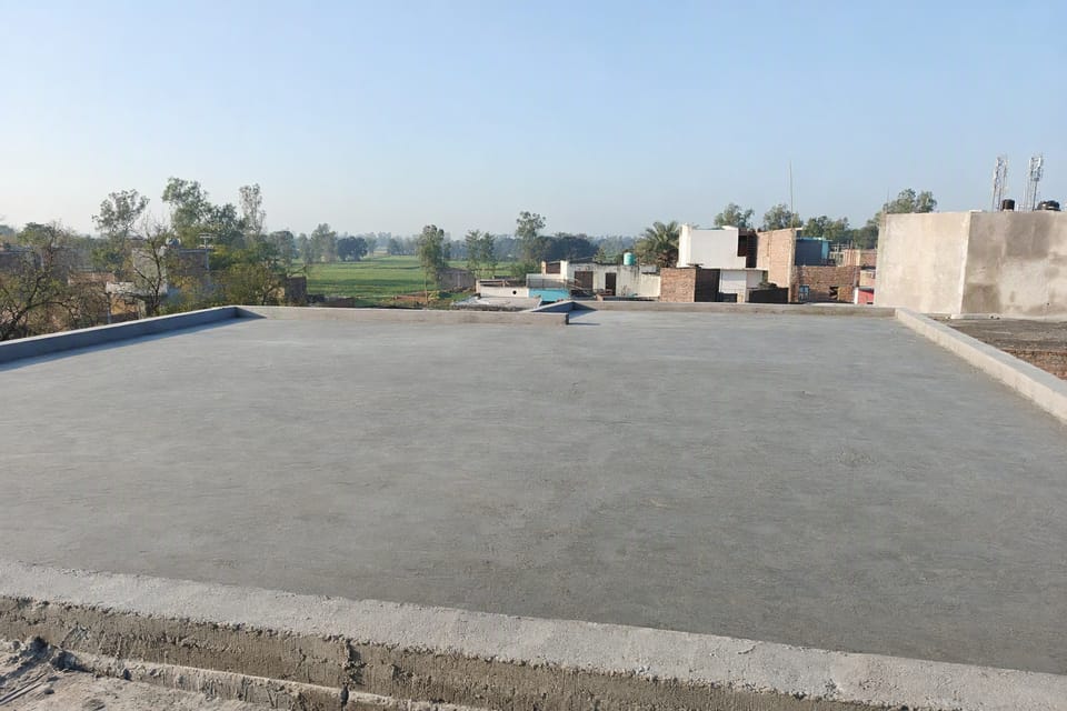 A level, freshly cast flat concrete roof slab with a low parapet and a clear sky behind