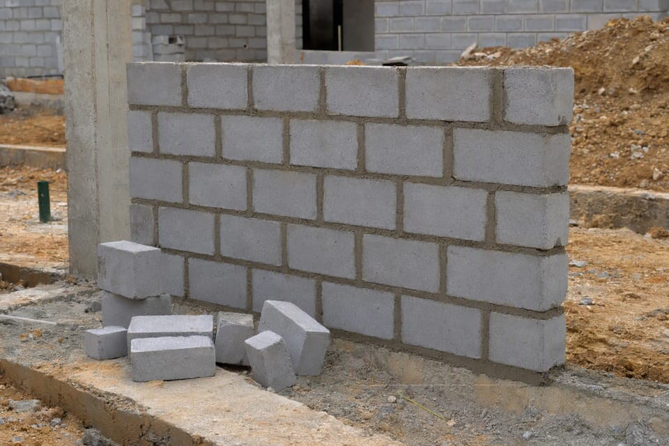 A partly built wall of grey masonry units with even mortar joints
