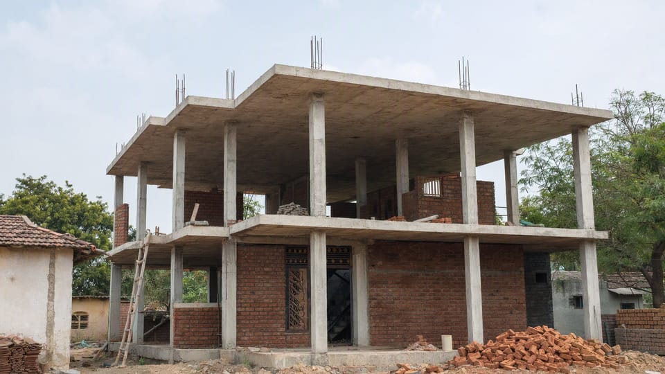 The shell of a two-storey Indian house with a concrete frame and partly built red brick infill walls