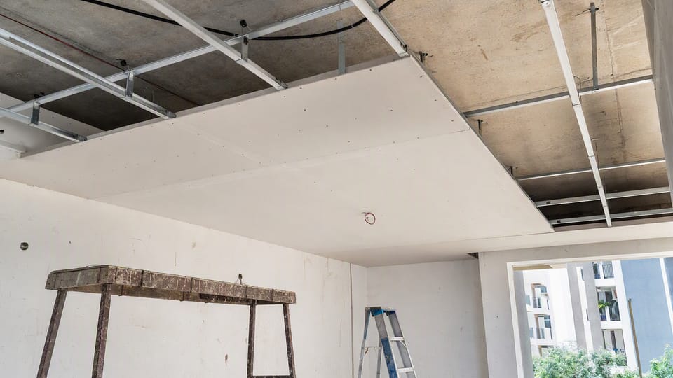A room under construction with a metal frame hung from the slab and white gypsum boards fixed to part of it