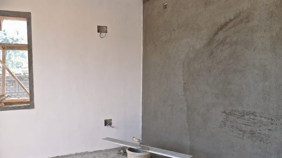 A room under construction with one wall in smooth white gypsum plaster and the next wall in grey cement plaster