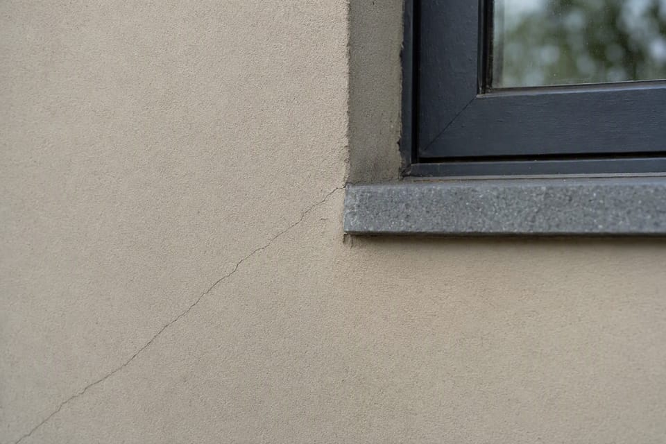 A very fine hairline crack running from the corner of a window on a plastered wall