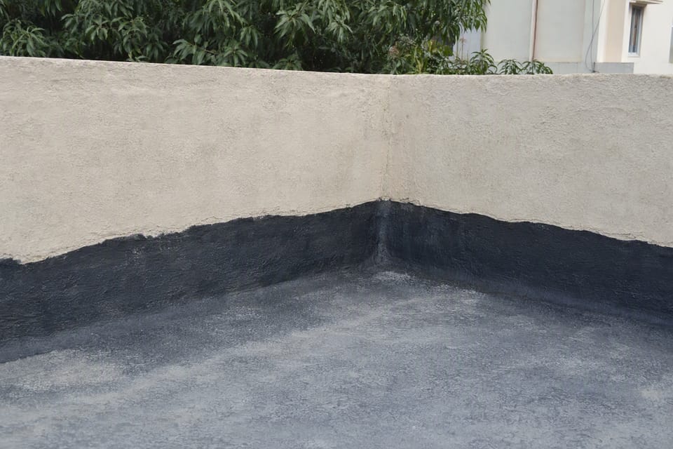 A dark waterproofing coat carried up the inside face of a plastered parapet wall at a corner