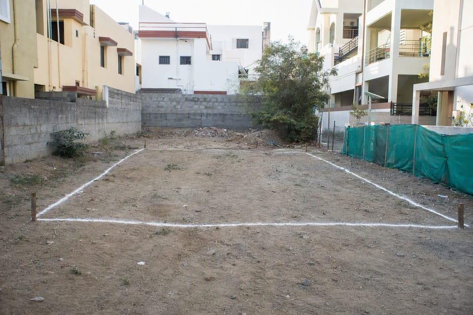 An empty plot in a town marked out with white lime lines and wooden pegs for a house