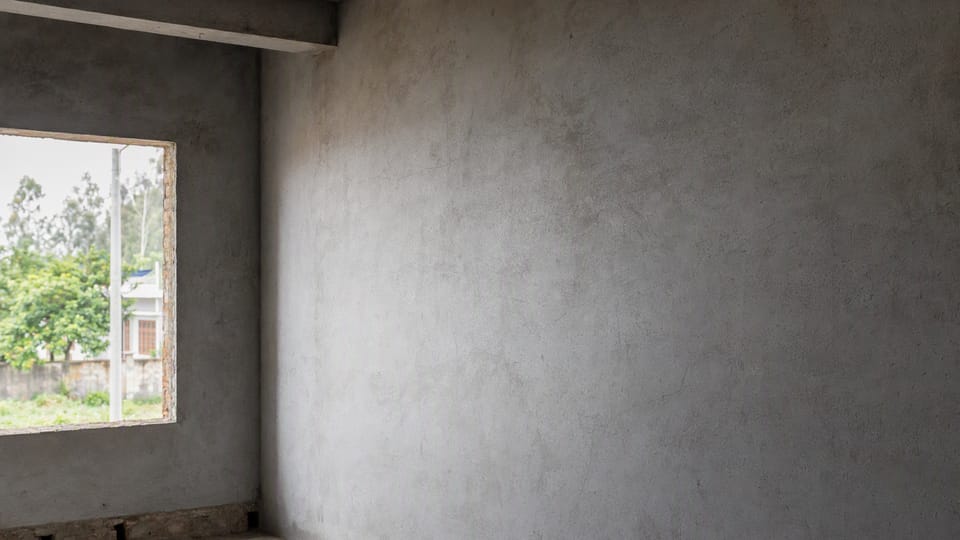 A grey cement plastered interior wall with a window in a house under construction