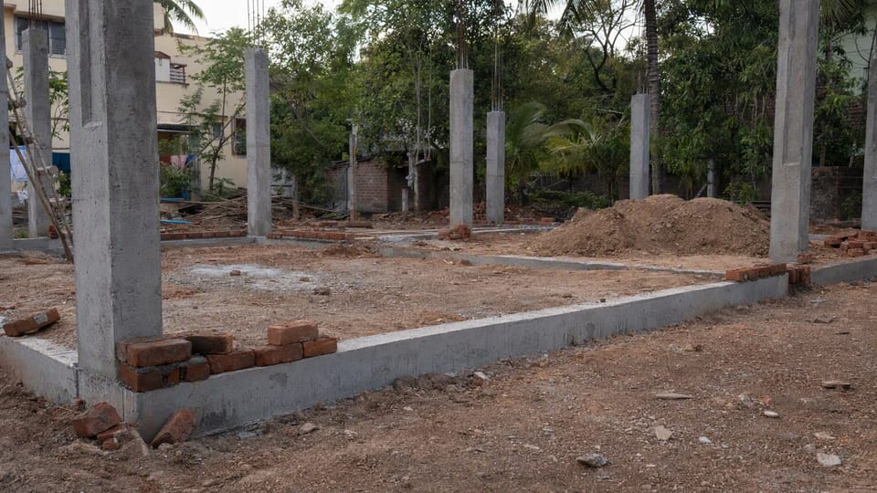 A grey concrete beam running at ground level between square concrete columns on a house plot with brick courses starting above
