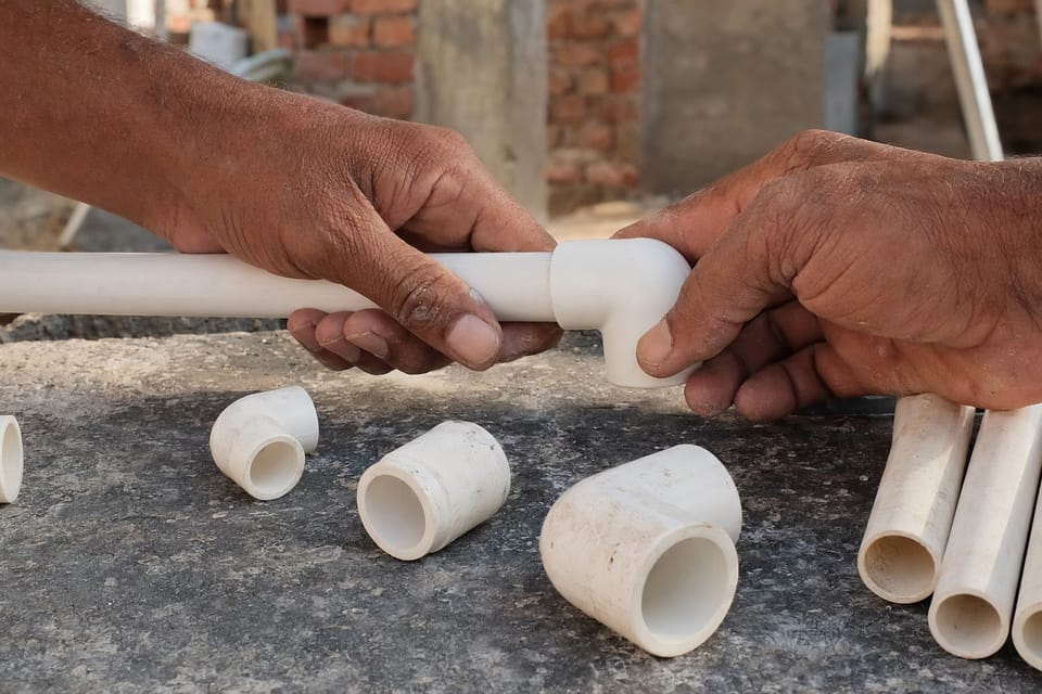 Two hands pushing a white plastic pipe into the socket of a matching elbow fitting on a workbench