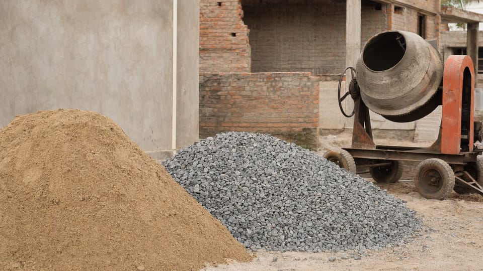 A heap of sand and a heap of crushed stone beside a drum concrete mixer on an Indian building site