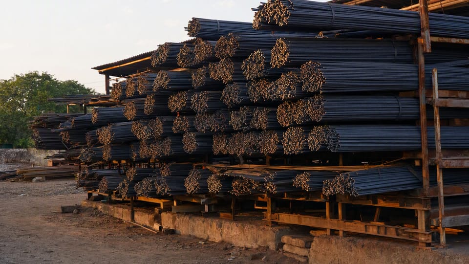 Bundles of ribbed steel reinforcement bars stacked on a rack in a building-material yard in warm light