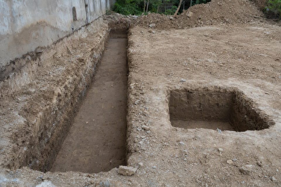 A long trench along a wall and a separate square pit on a building plot, ready for footings