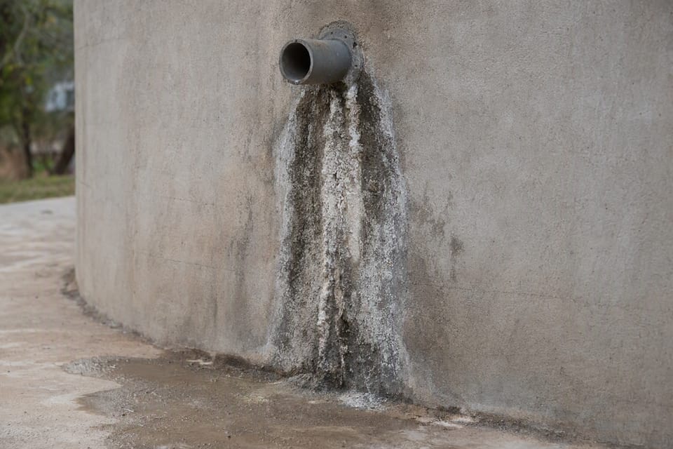 A damp stain and white salt marks on the outer wall of a concrete tank below a pipe connection