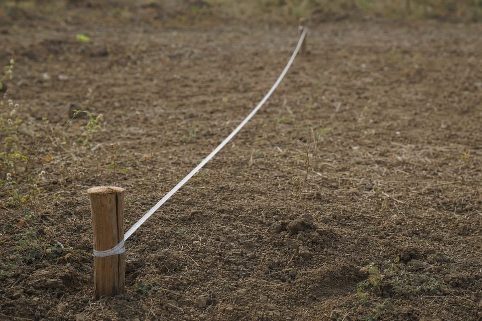 A long measuring tape stretched along the ground between two wooden pegs on a plot