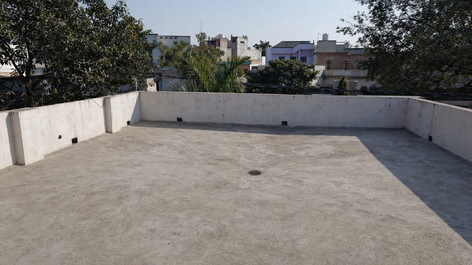 A clean dry flat concrete terrace of an Indian house with a low parapet and a round rainwater outlet at a low point